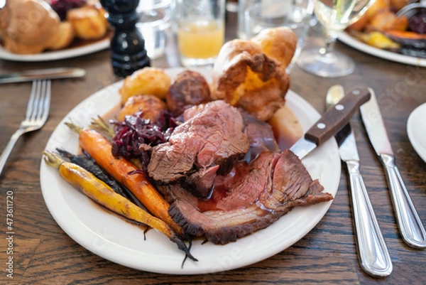 Fototapeta Roast beef on a white plate with roast potatoes and Yorkshire pudding with vegetables in a restaurant.