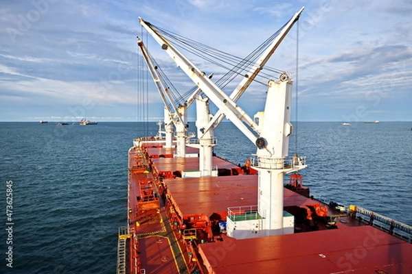 Fototapeta Loading coal from cargo barges onto a bulk carrier using ship cranes and grabs at the port of Muara Pantai, Indonesia. January,2021.