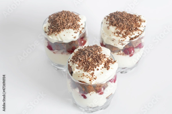 Fototapeta Biscuit cake with cream and cherries in a glass on a white background