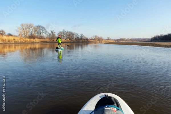 Fototapeta Late autumn on a clear day a man is rafting on a supboard on the river. SUP. Stand up paddle boarding