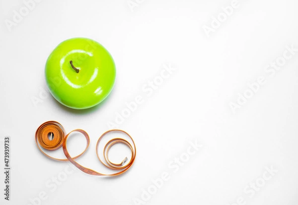 Fototapeta Healthy and healthy snack: green apple and measuring tape, diet and sports on a white background with space for text. The concept of a healthy lifestyle, top view