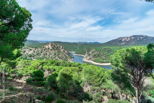 Fototapeta Forest landscape of pine forests, mountains and lake with a sky full of clouds. View of "Pantano de San Juan in San Martin de Valdeiglesias, Madrid"