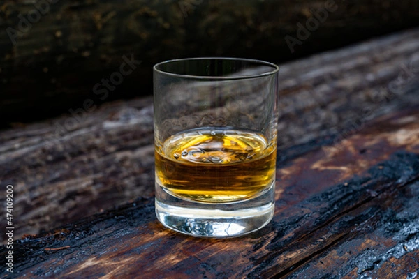 Fototapeta Glass of strong scotch single malt whisky on old log soaked in creosote