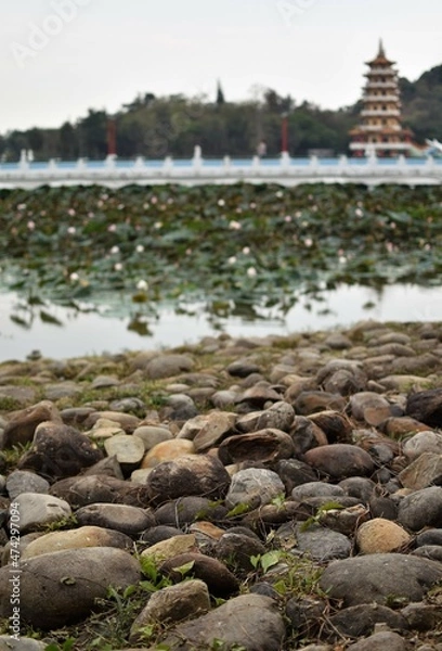 Fototapeta Pebbles and stones at the bank of a river with a majestic pagoda in the background