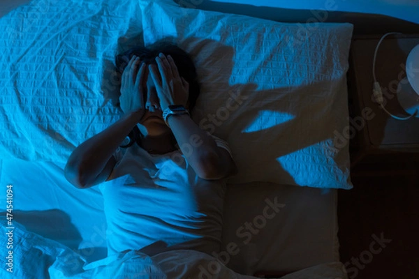Fototapeta Beautiful girl suffering from insomnia lying in her bed in the middle of the night. Hands in her face.