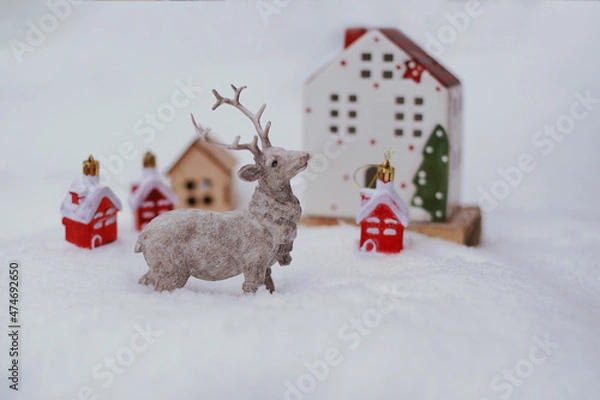 Fototapeta The figure of a deer, toy houses, fir branches in the snow.