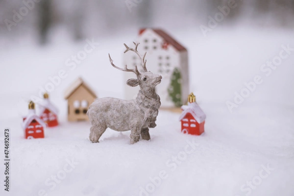 Fototapeta The figure of a deer, toy houses, fir branches in the snow.