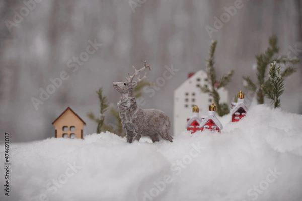 Fototapeta The figure of a deer, toy houses, fir branches in the snow.