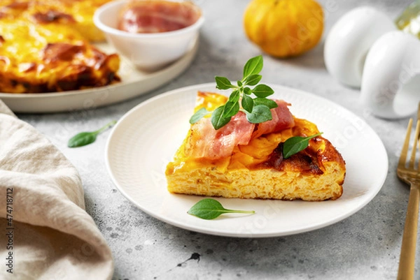 Obraz A piece of frittata with pumpkin, bacon and ricotta in a ceramic plate on a light culinary background. Traditional Italian delicious homemade egg dish on the kitchen table closeup	