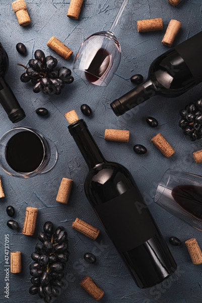 Fototapeta Wineglasses with red wine,black grape,wine corks and lying bottle on black stone desk. Top view.