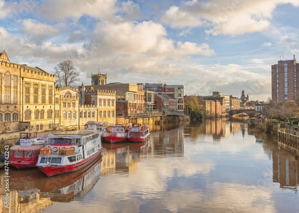 Fototapeta A winter sun falls up on the 15th Century Guildhall in York.  The sky and clouds are reflected in the water and a bridge is in the distance.
