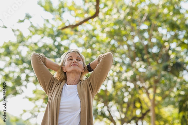 Fototapeta Portrait photo of happy senior Caucasian woman relaxing and breathing fresh air with sunlight in outdoors park. Elderly woman enjoying a day in the park on summer. Healthcare lifestyle and wellness 