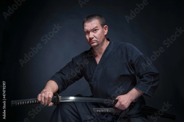 Fototapeta A man in a samurai kimono holding a katana in his hands on a black background, studio session