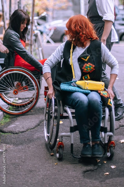 Fototapeta Waiters lift a girl in a wheelchair up the steps without a ramp. A woman is going to have lunch in a cafe inaccessible to people with special needs