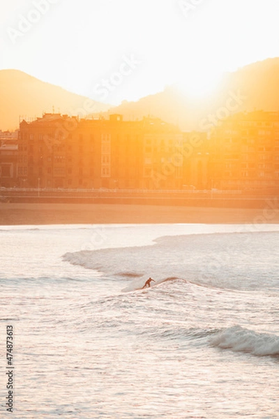 Fototapeta Silhouette of a lonely surfer riding a wave during sunset in San Sebastian beach