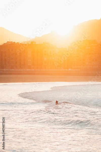 Fototapeta Silhouette of a lonely surfer riding a wave during sunset in San Sebastian beach