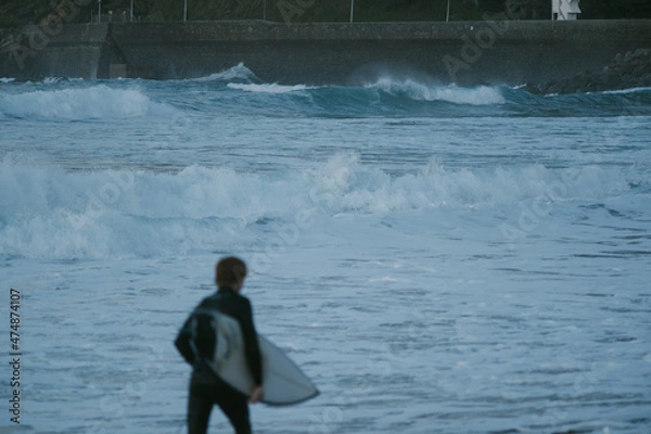 Fototapeta Blurry young surfer running in front of the ocean during sunset