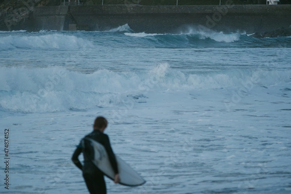 Fototapeta Blurry young surfer running in front of the ocean during sunset