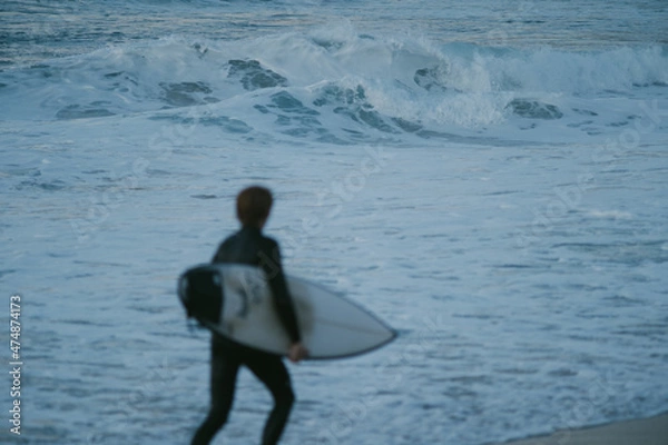 Fototapeta Blurry young surfer running in front of the ocean during sunset