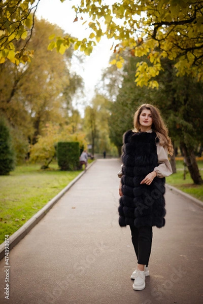 Fototapeta photo session of the girl in the park in autumn. back light. girl stands near a yellow tree on the sidewalk. full-length portrait of a girl with background.