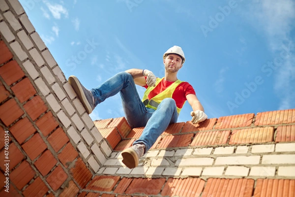 Fototapeta Bottom view of worker sitting at brick wall