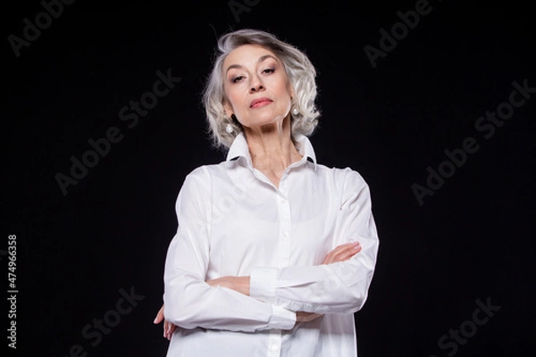 Obraz Portrait of a domineering, arrogant mature woman looking down and standing with her arms crossed isolated on a black background