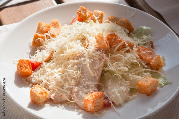 Fototapeta Appetizing caesar salad with bacon, croutons and cheese on a white plate in a restaurant