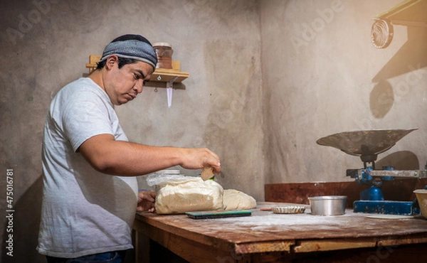 Fototapeta Latin baker weighing a ball of bread dough on a scale to then put it in the oven