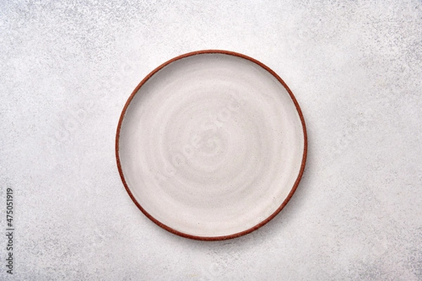 Fototapeta Empty white ceramic plate with brown rim on a light textured background, top view, copy space