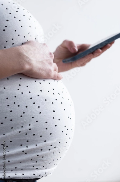 Obraz A pregnant woman stands in the background of a window using a phone