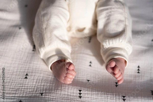Obraz Charming legs of a newborn baby lying on a bright bed in the light of the bright sun
