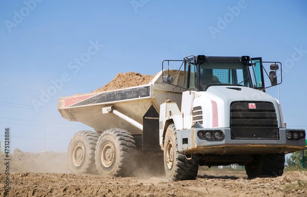 Fototapeta large gray articulated dumper at a construction site drives down a dusty road . loading and transportation of soil.
