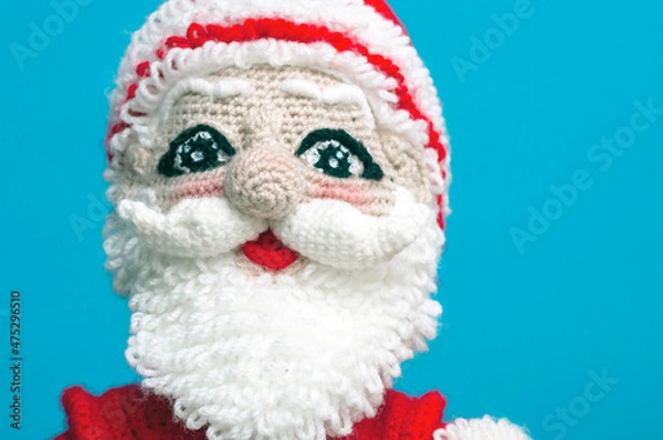 Fototapeta the face of a knitted Santa Claus toy on a blue background close-up.