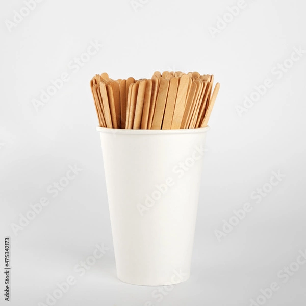 Fototapeta Wooden coffee sticks in a paper disposable cup. On white background
