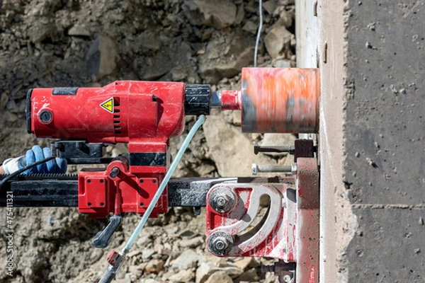 Fototapeta Worker is drilling to concrete wall with core drill machine. Core drills used in metal are called annular cutters. Core drills used for concrete and hard rock generally use industrial diamond grit.