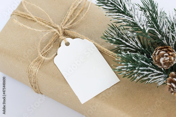 Fototapeta Christmas and New Years background close-up. Gift box wrapped in kraft paper with jute cord. Decorated with a label and a branch with cones