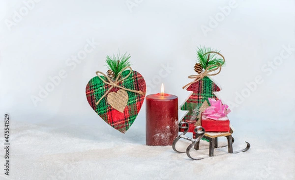 Fototapeta Christmas composition: a handmade heart, a toy sleigh with a gift and a candle on the background of a toy Christmas tree. Selective focus