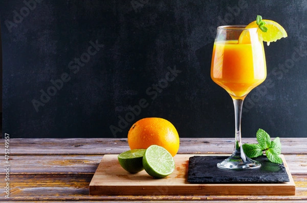 Obraz Glass of orange and lime juice with mint on wooden table with natural orange and lime accompanying with black background