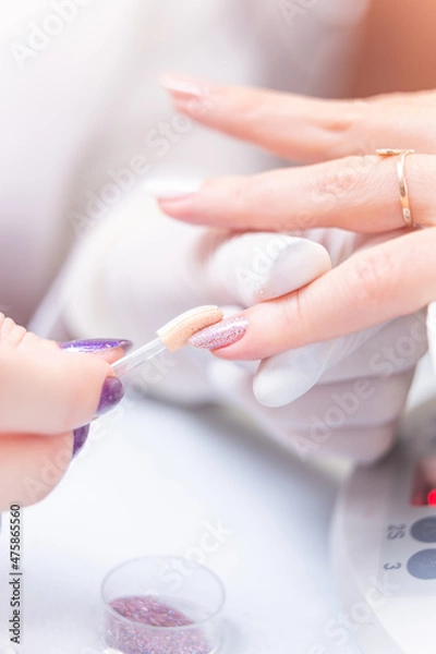 Fototapeta applying bright glitter on a customer's nails in a beauty studio