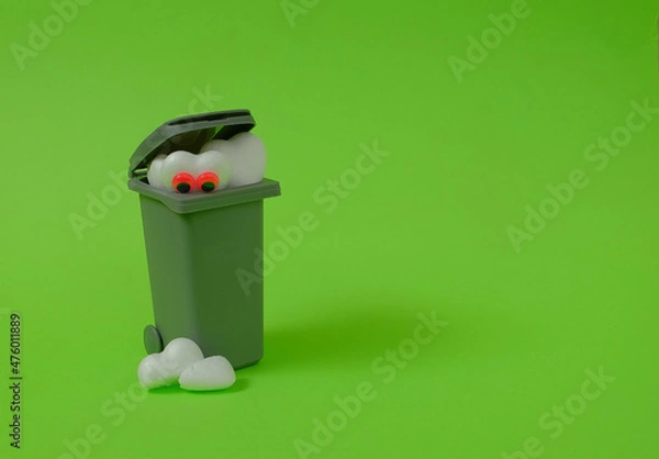 Fototapeta A trash can, a white heart with eyes looking at a broken heart at the bottom on a bright green background. Text space. Broken heart, rejection, waste concept. Minimal style.