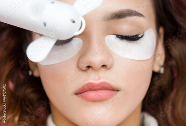 Obraz Eyelash extensions. a young woman undergoes a close-up eyelash extension procedure. The master dries the eyelashes after the procedure with a fan.