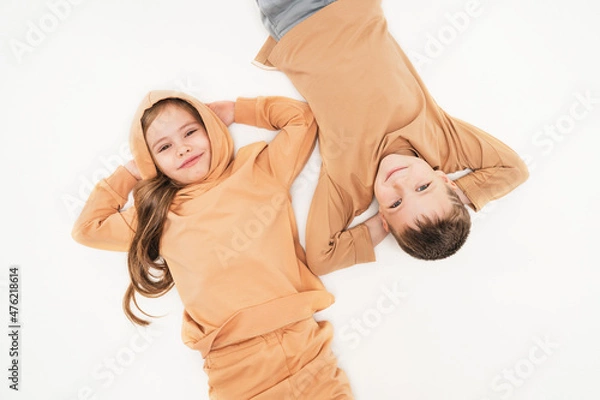 Fototapeta Children in sportswear lie on the floor and look into the frame. Friendship of a boy and a girl since childhood. The brother and sister put their hands behind their heads and rested.