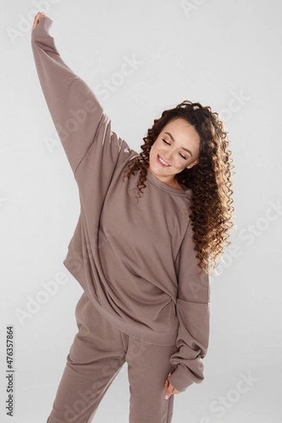Obraz Young happy female model with afro hairstyle and closed eyes wearing blanked grey hoodie and pants smiling and posing over white background