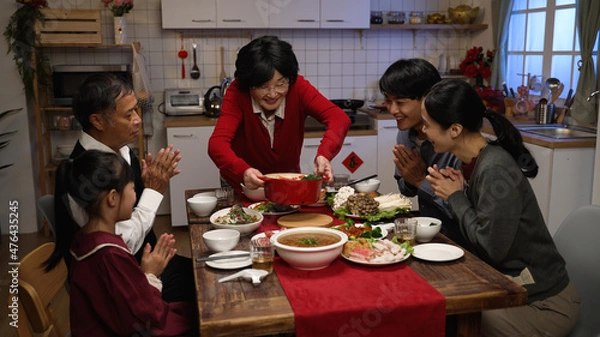 Obraz happy grandmother serving delicious food on dining table as her family members clapping hands for her. getting ready for big meal on chinese new year's eve