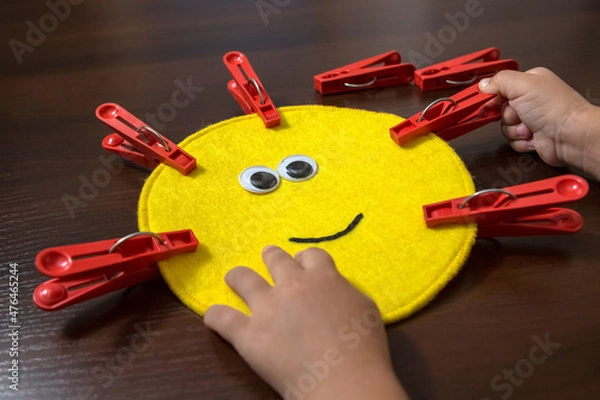Obraz Hands of a little girl preschool age. Lesson with a colored die and clothespins. Sensory development, Fine motor skills, Montessori method, Tools, Child development concept.