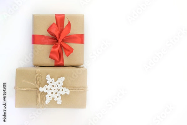 Fototapeta Christmas and New Years flatlay background. Gift box wrapped in kraft paper with jute cord. Decorated with a crocheted snowflake. Box with a red ribbon. Place for your text