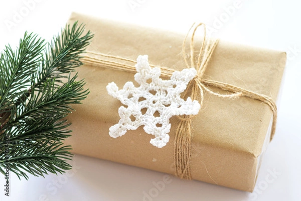 Fototapeta Christmas and New Years background close-up. Gift box wrapped in kraft paper with jute cord. Decorated with a crocheted snowflake and a branch