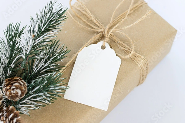Fototapeta Christmas and New Years background close-up. Gift box wrapped in kraft paper with jute cord. Decorated with a label and a branch with cones