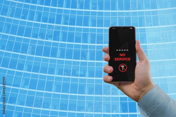 Fototapeta A man's hand holds a smartphone with the notification 'No service' against the background of a business building with a blue glass facade. Notification 'No service' on the smartphone screen
