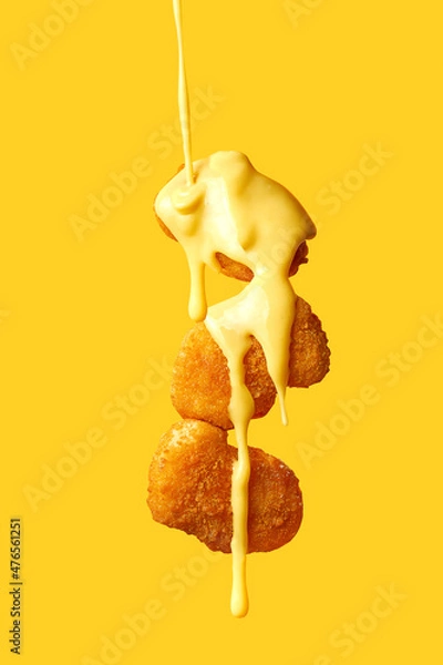 Fototapeta Levitating chicken nuggets topped with cheese sauce. Flying nuggets with flying sauce. Yellow background